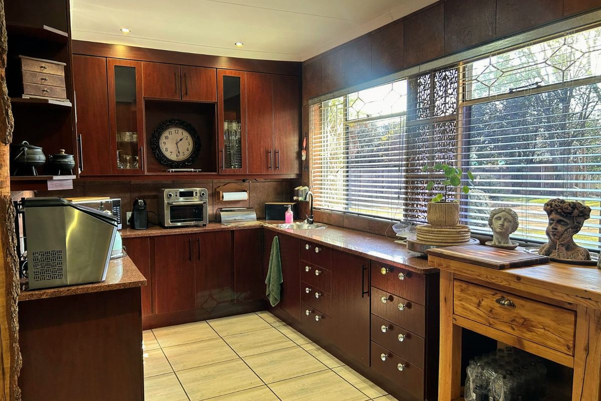 A well-maintained kitchen featuring dark wood cabinetry, granite countertops, tiled flooring, and a large window providing ample natural light.