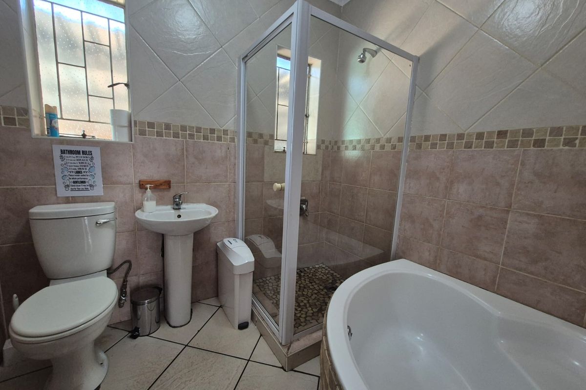 A functional bathroom featuring a corner bathtub, separate shower enclosure, pedestal basin, and toilet with neutral tiled finishes.