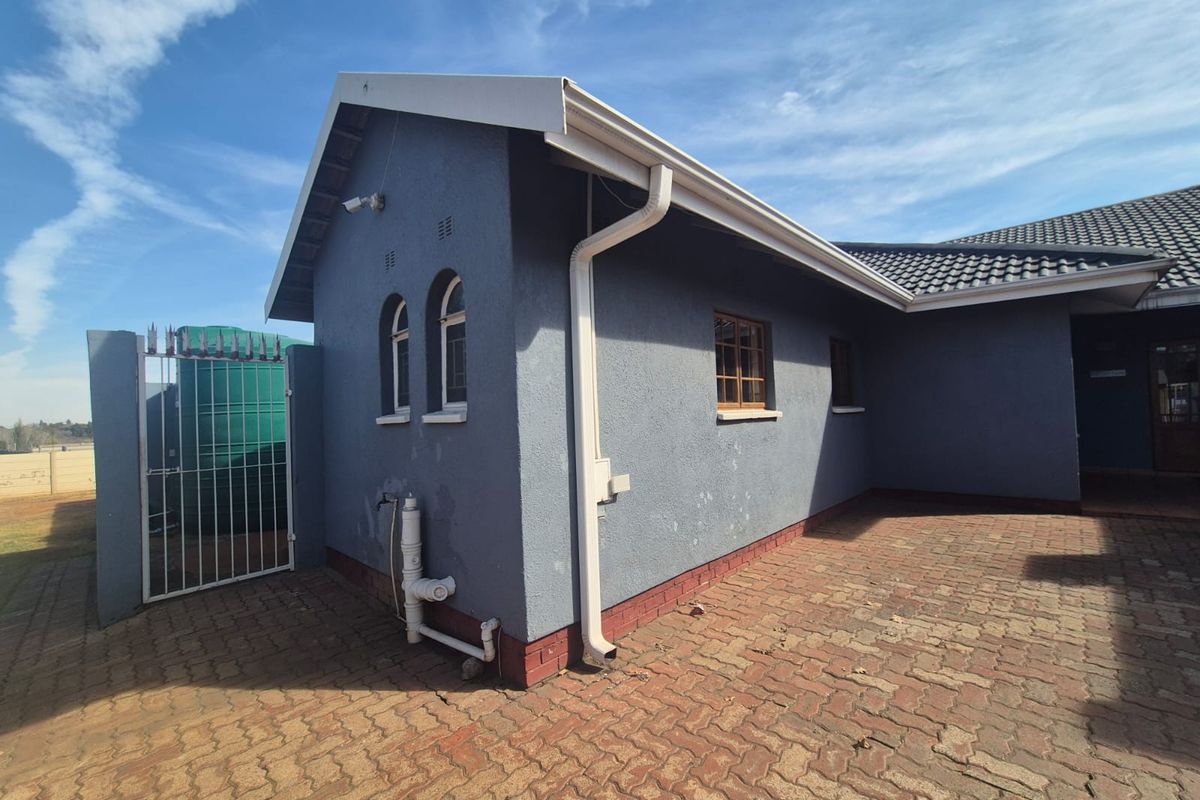 Rear exterior view of the house featuring paved courtyard, arched windows, and functional rainwater drainage system.