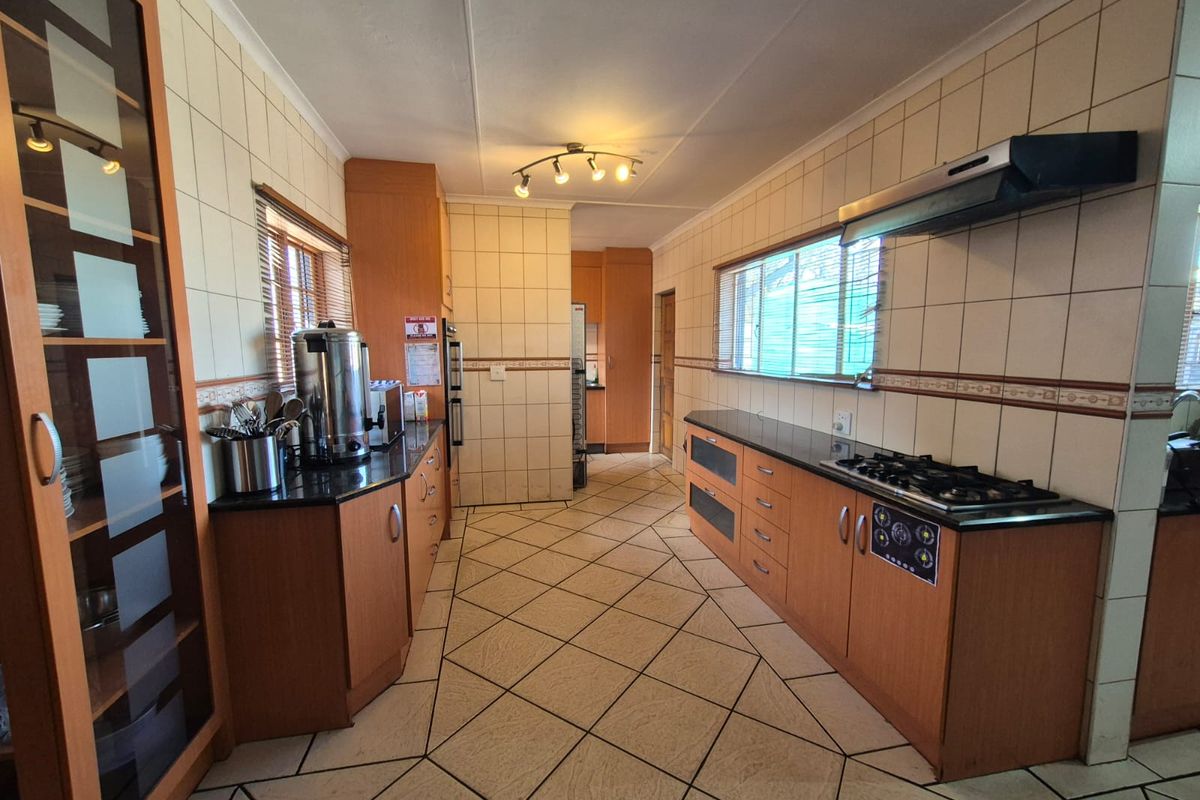 A functional kitchen featuring wooden cabinetry, granite countertops, a gas hob with extractor fan, and tiled finishes throughout.