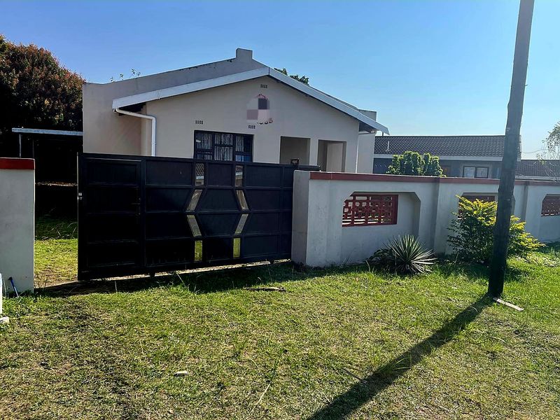 Front exterior view of a single-story house featuring a metal driveway gate, perimeter wall, and tiled roof.