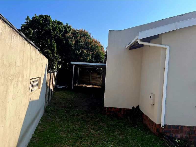 A view of the rear exterior area showing a side boundary wall, a carport structure, and the rear facade of the house.