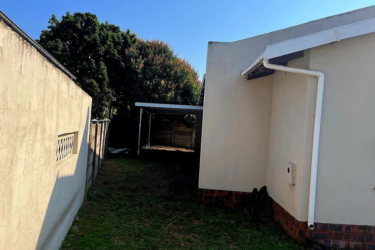 A view of the rear exterior area showing a side boundary wall, a carport structure, and the rear facade of the house.