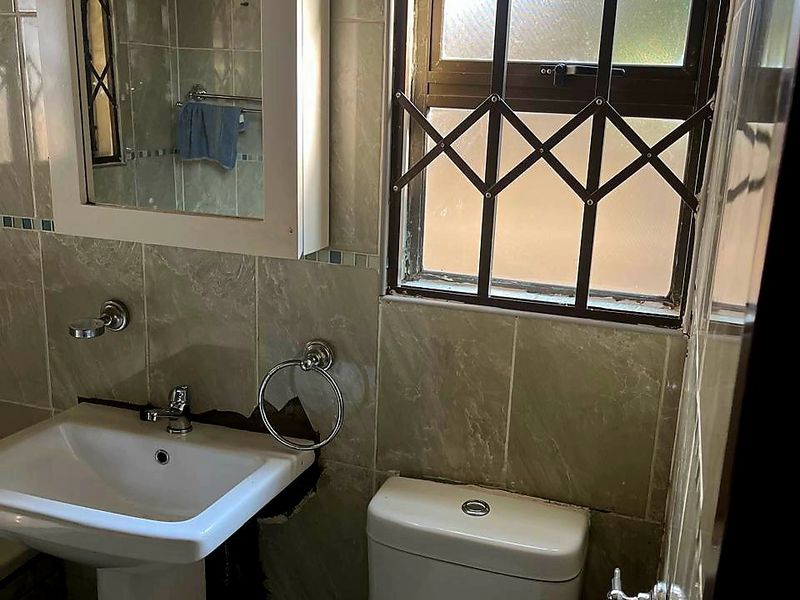 A compact bathroom featuring a pedestal basin, toilet, and tiled walls, currently requiring repair to the tiling behind the basin.