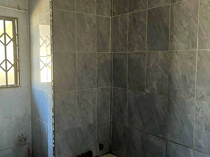 A bathroom featuring a bathtub with grey marble-effect wall tiles and tiled flooring, requiring minor finishing work to the tile edges.