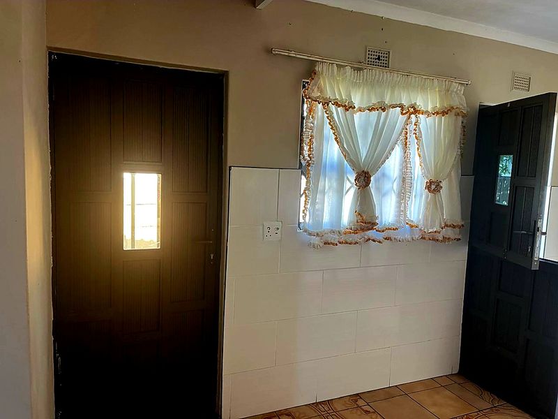 A functional kitchen area featuring ceramic floor tiles, tiled wall splashbacks, and direct access to exterior doors.