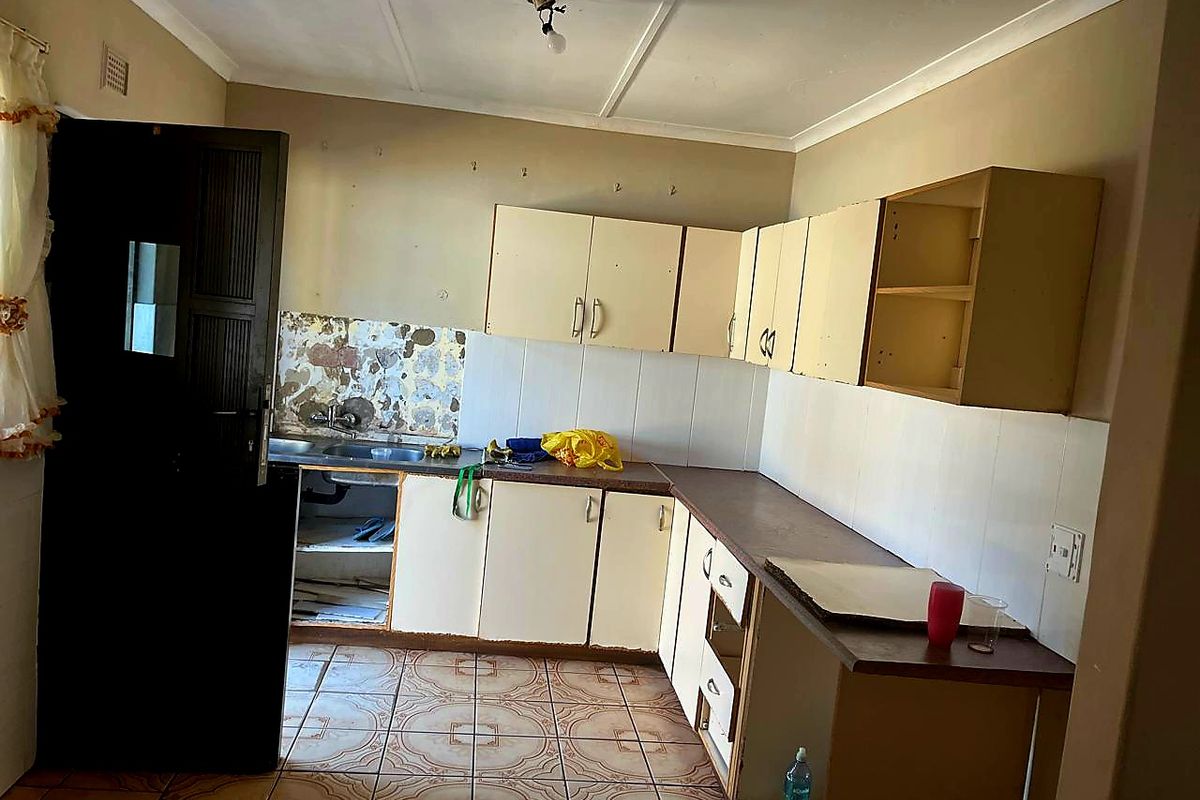 A dated kitchen featuring built-in cabinetry, laminate countertops, and tiled flooring, currently in need of renovation and cosmetic updates.