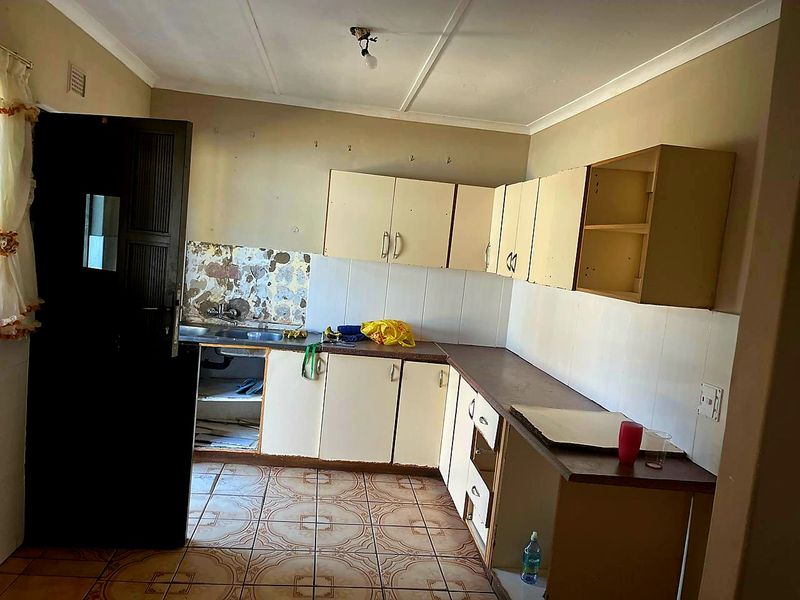 A dated kitchen featuring built-in cabinetry, laminate countertops, and tiled flooring, currently in need of renovation and cosmetic updates.