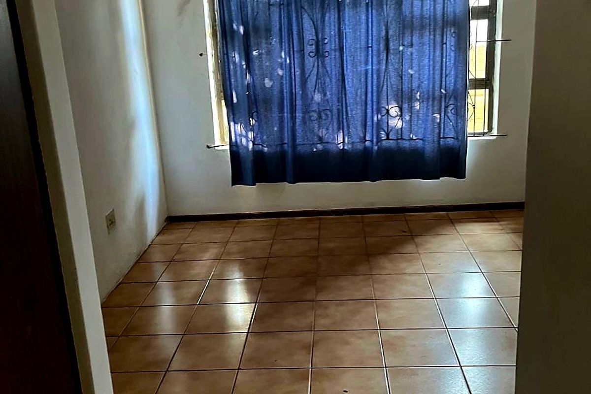 An empty bedroom featuring ceramic floor tiles, security burglar bars on the window, and a built-in cupboard.
