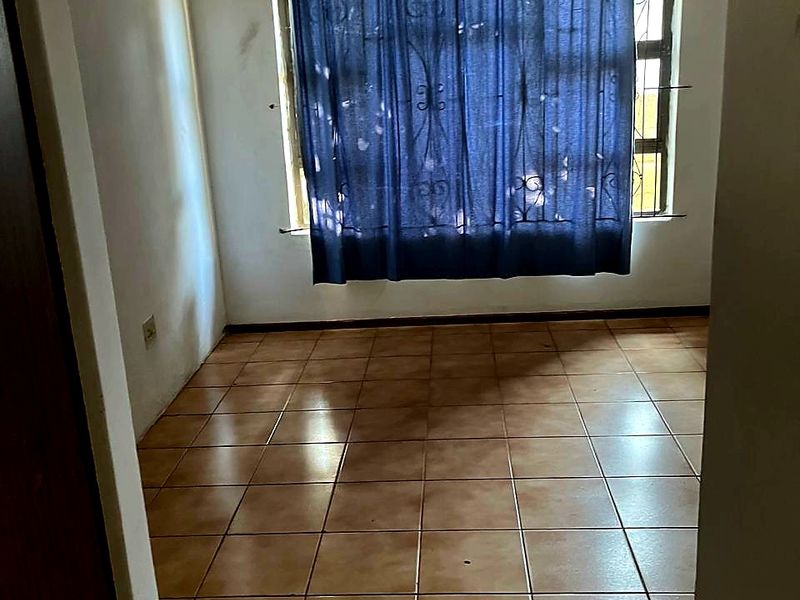 An empty bedroom featuring ceramic floor tiles, security burglar bars on the window, and a built-in cupboard.