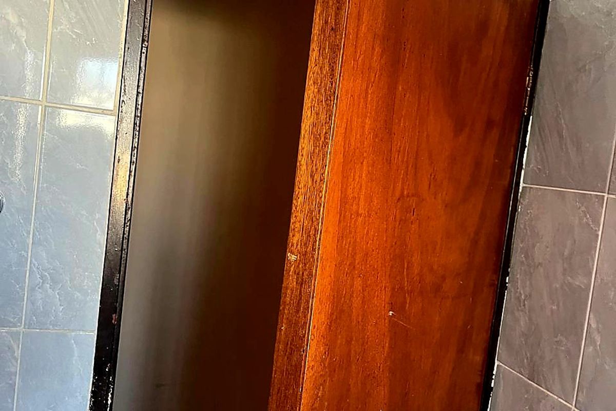 A close-up view of a bathroom doorway featuring blue ceramic wall tiles and a worn timber door requiring maintenance or replacement.