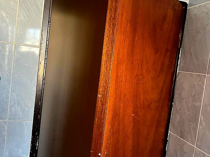 A close-up view of a bathroom doorway featuring blue ceramic wall tiles and a worn timber door requiring maintenance or replacement.