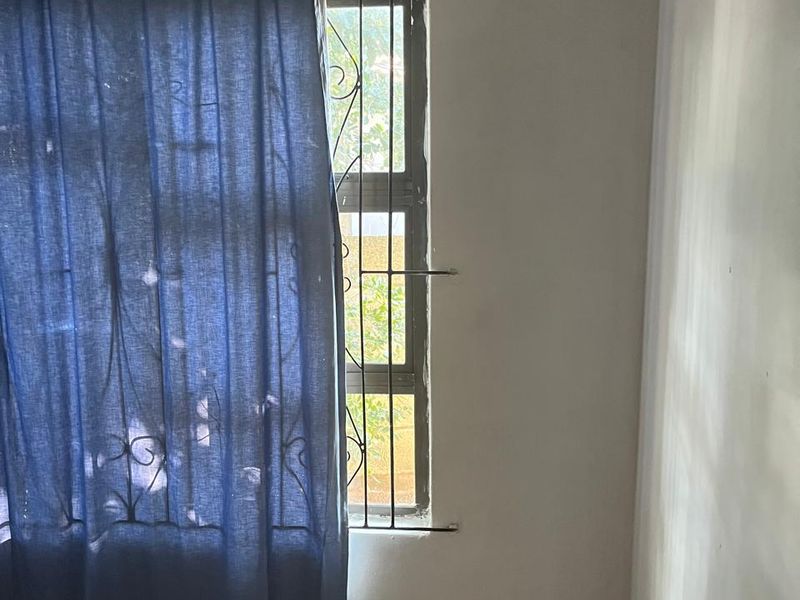 An empty bedroom featuring tiled flooring, a window with security bars, and a wall-mounted air vent.