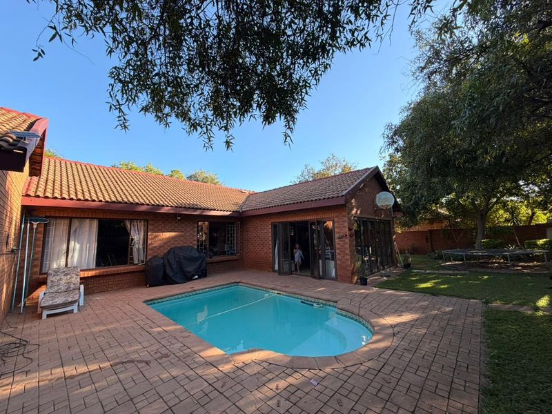 A rear exterior view featuring a swimming pool, brick paved patio area, and direct access to the home through sliding glass doors.