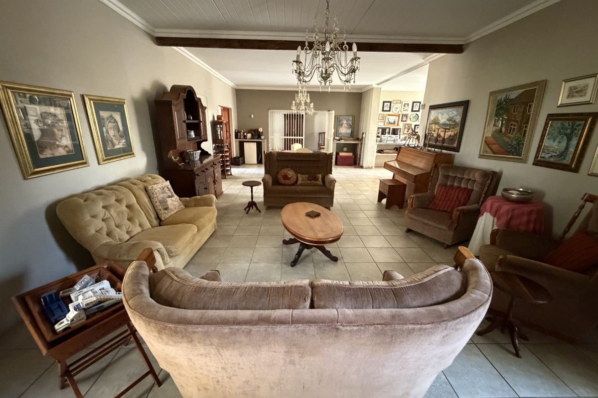 Spacious living area featuring tiled flooring, exposed ceiling beams, and a classic chandelier, offering a traditional layout with ample room for seating.