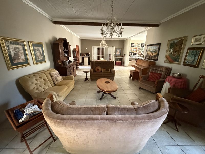 Spacious living area featuring tiled flooring, exposed ceiling beams, and a classic chandelier, offering a traditional layout with ample room for seating.