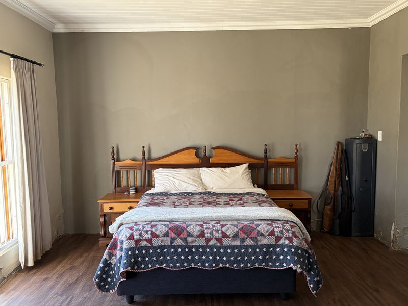A bedroom featuring laminate flooring and a tongue and groove ceiling, currently showing signs of wear on the lower wall surfaces.
