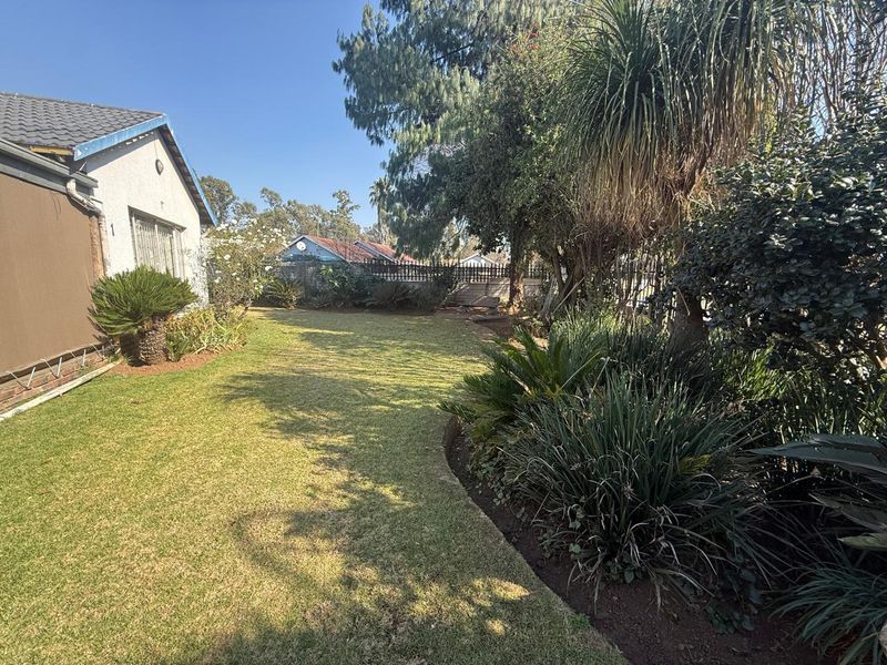 A well-maintained rear garden featuring a manicured lawn, established garden beds, and secure perimeter walling.