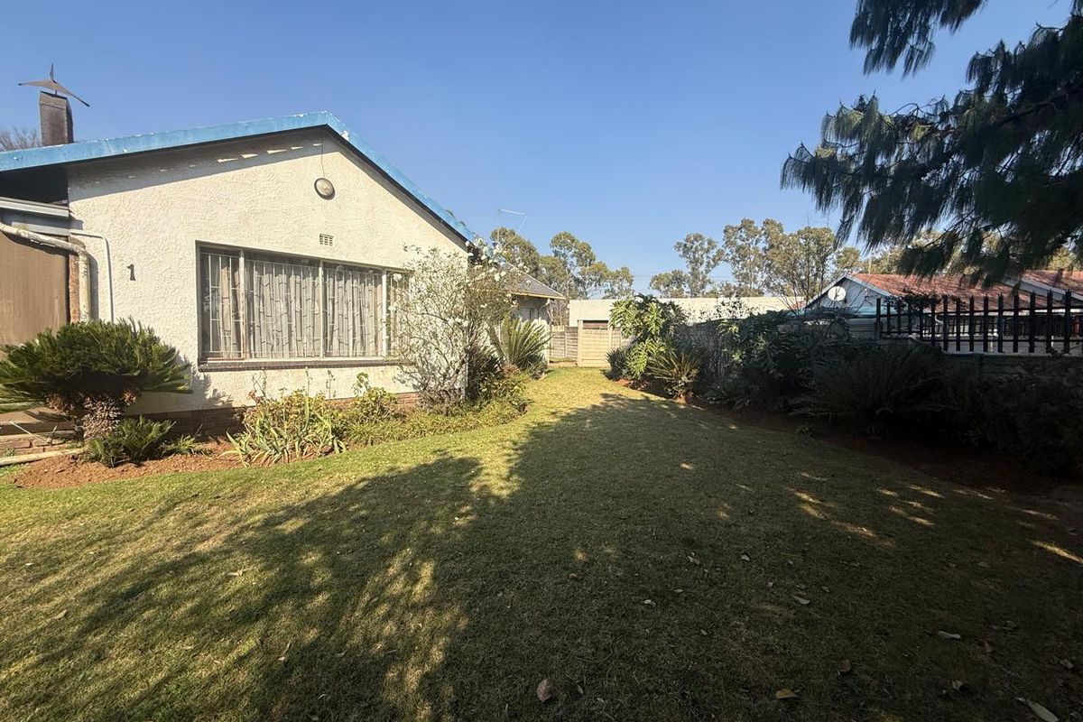 A view of the rear garden featuring a lawn, established landscaping, and boundary walling, with the rear elevation of the house visible.
