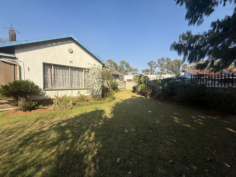 A view of the rear garden featuring a lawn, established landscaping, and boundary walling, with the rear elevation of the house visible.