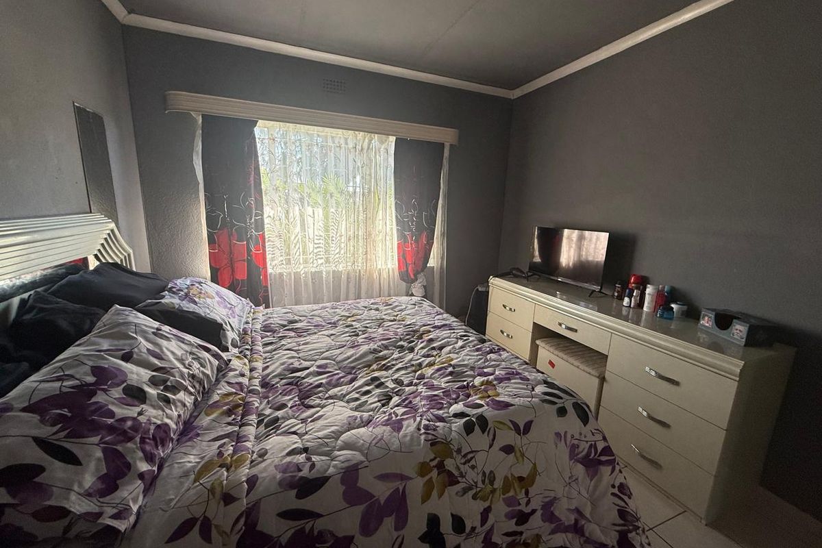 A standard bedroom featuring tiled flooring, dark grey walls, and window security bars, providing a functional living space.