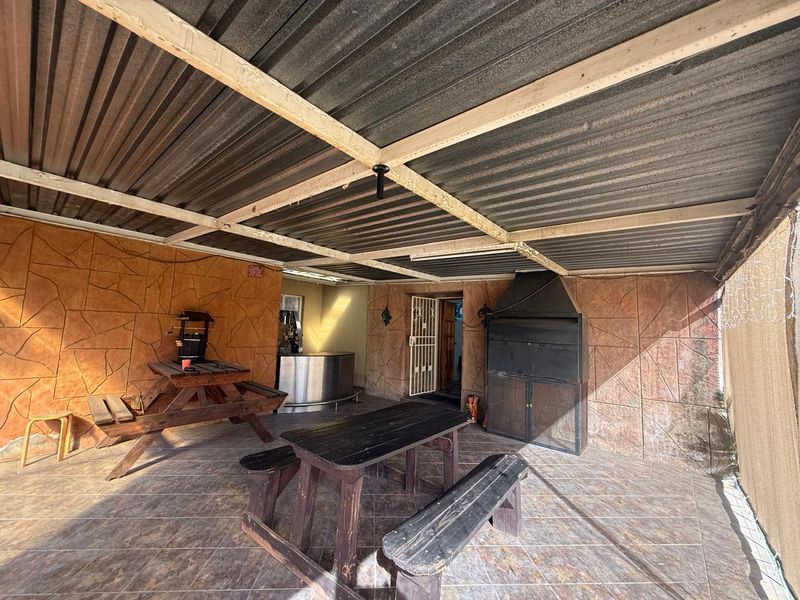 Covered outdoor patio area featuring a built-in braai, stone-cladding wall finish, and tiled flooring, providing a functional space for outdoor entertainment.