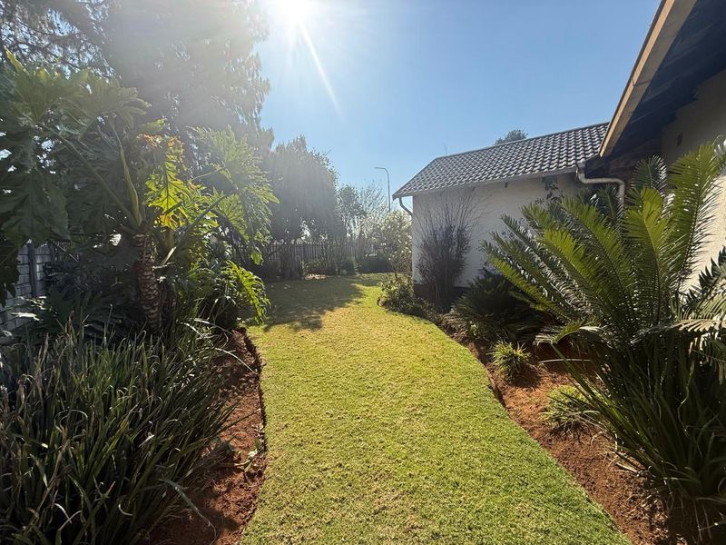 A well-maintained rear garden featuring a manicured lawn, established tropical landscaping, and a clear view of the property's side elevation and roofline.