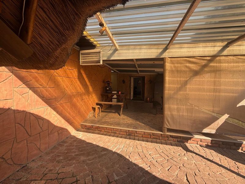 Covered outdoor patio area featuring a combination of thatched and corrugated roofing, brick paving, and tiled flooring with wall-mounted air conditioning.