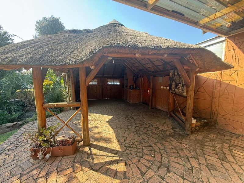 A rustic outdoor entertainment area featuring a traditional thatch roof, timber support structure, and paved flooring, ideal for relaxed outdoor living.