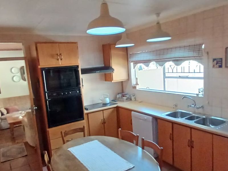 A functional kitchen featuring wooden cabinetry, built-in eye-level oven, double sink, and tiled splashbacks, offering a classic layout with potential for modern updates.