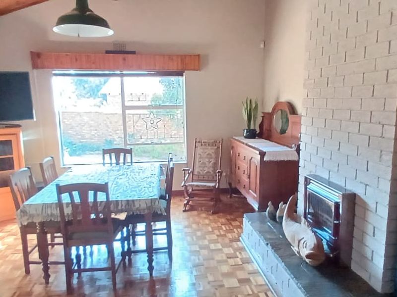 Open plan living and dining area featuring a brick fireplace, parquet flooring, and a vaulted timber ceiling with natural light.