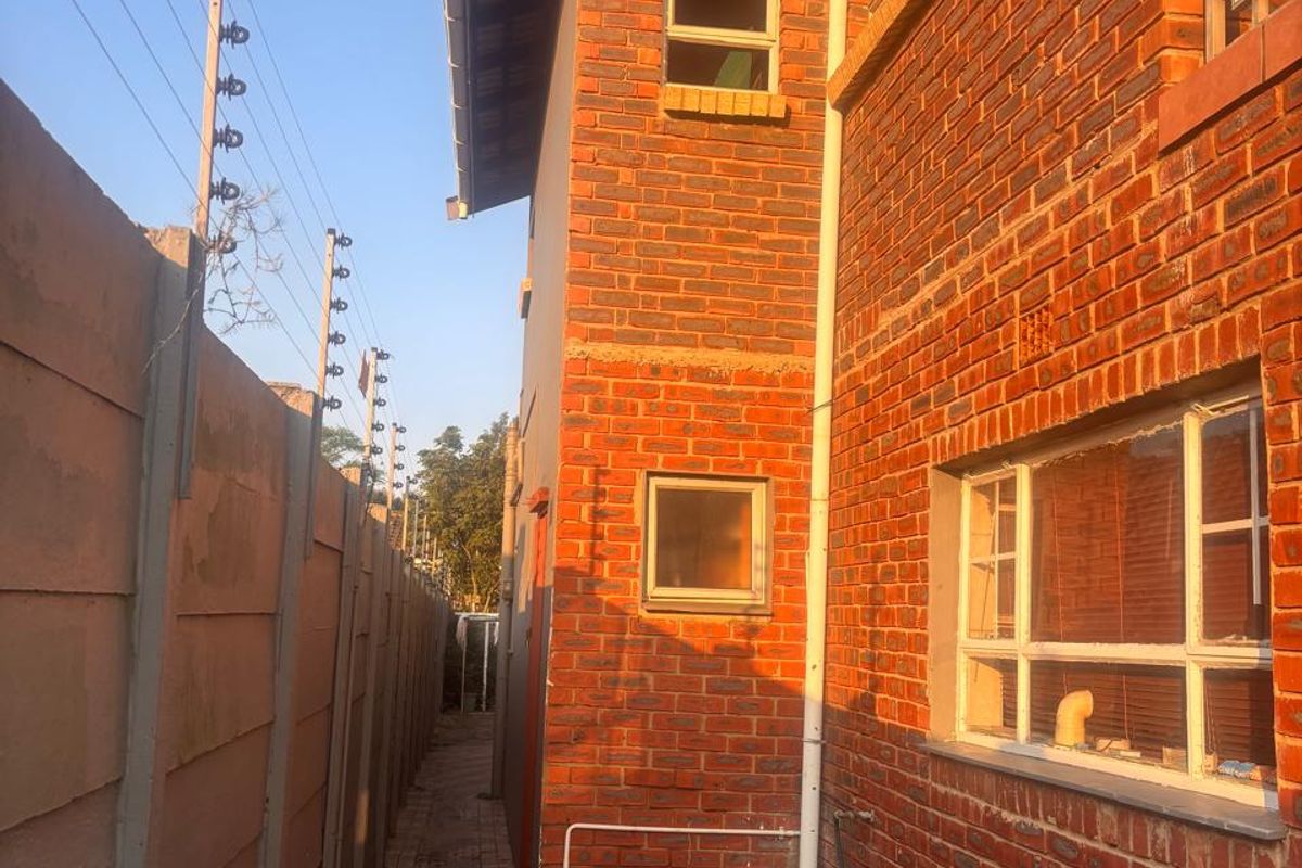 Side exterior view of the property featuring face brick construction, paved walkway, and secure boundary wall with electric fencing.