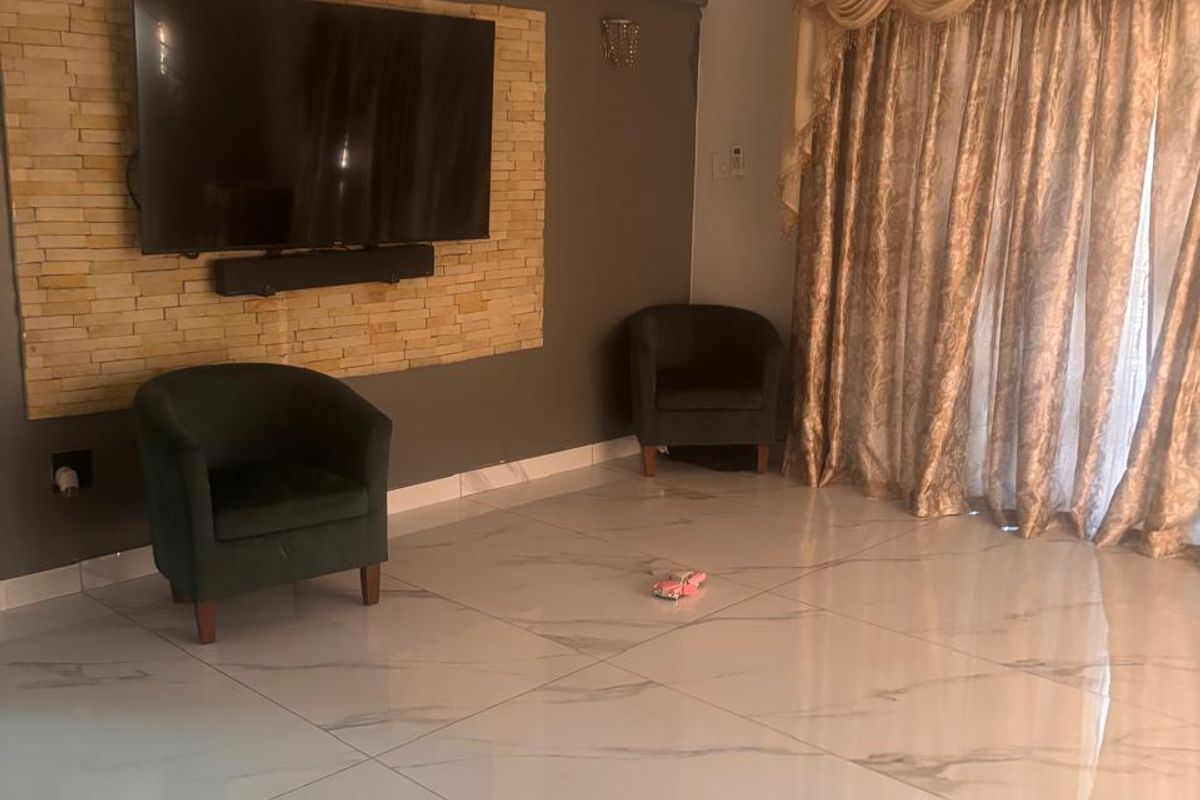 Spacious living room featuring polished marble-look floor tiles, a stone feature wall with mounted television, and a modern ceiling fan.