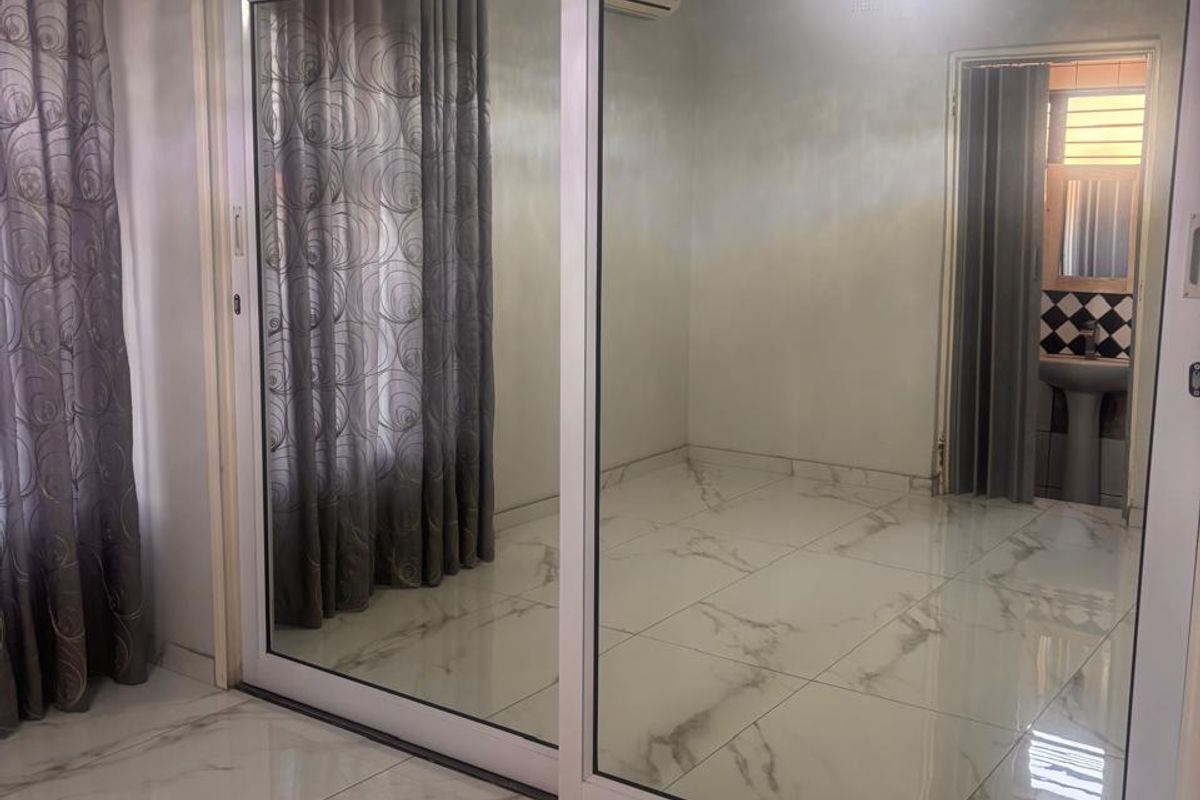 Spacious bedroom featuring large built-in mirrored sliding wardrobes with overhead storage, marble-look tiled flooring, and a wall-mounted air conditioning unit.