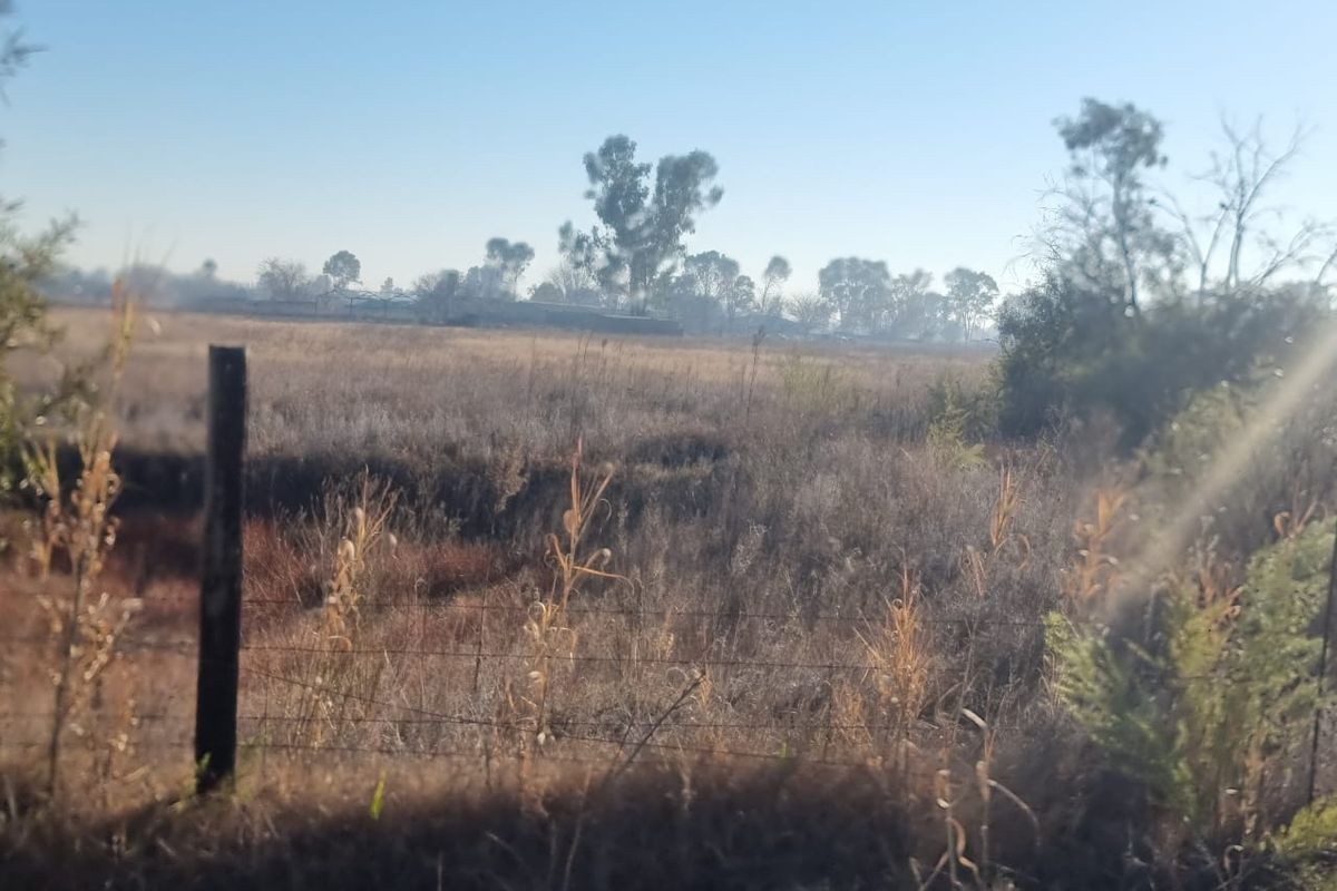 A view of an open, undeveloped residential land plot featuring dry vegetation and a wire boundary fence.