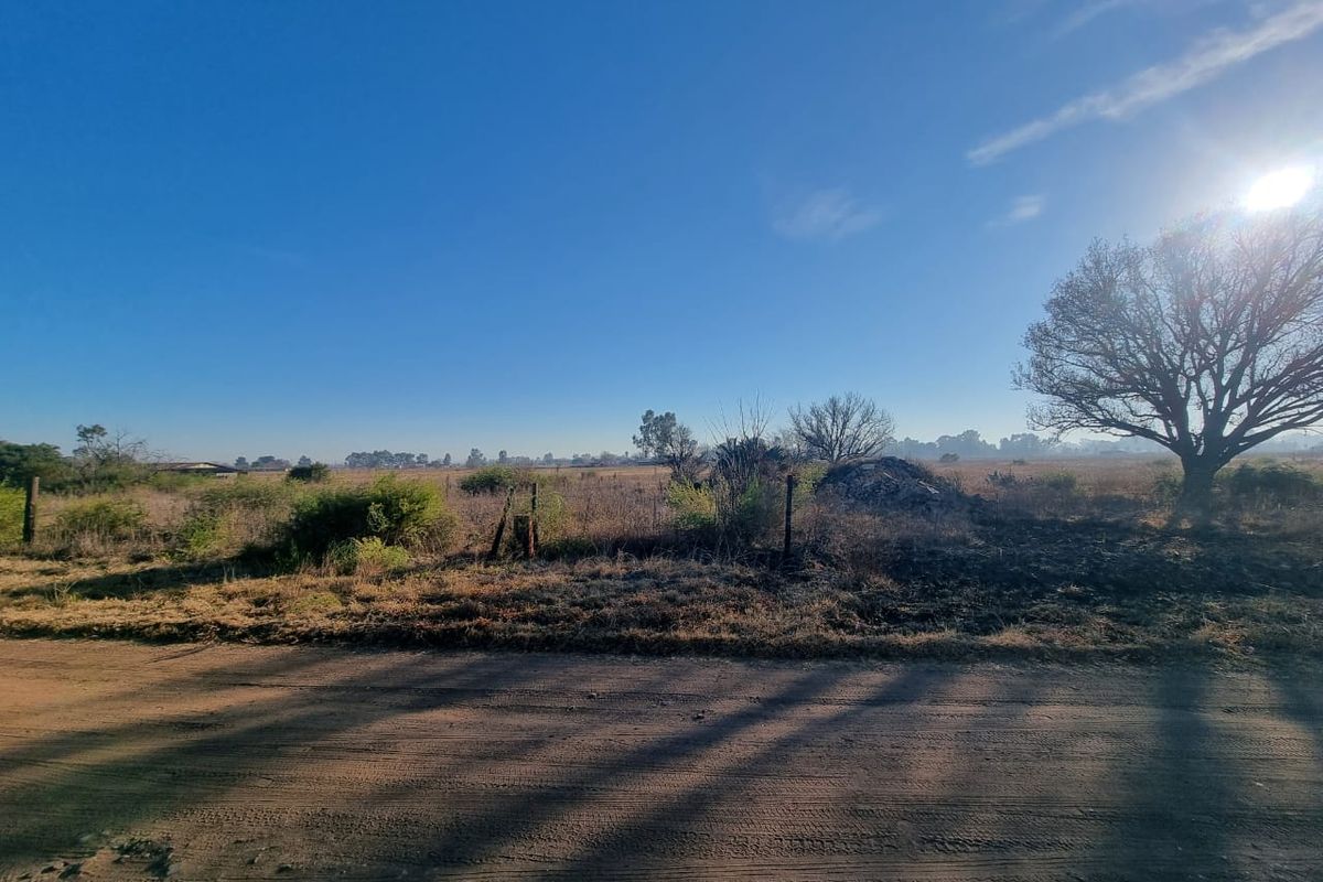 A view of the vacant residential land from the adjacent dirt road, featuring natural vegetation and perimeter wire fencing.