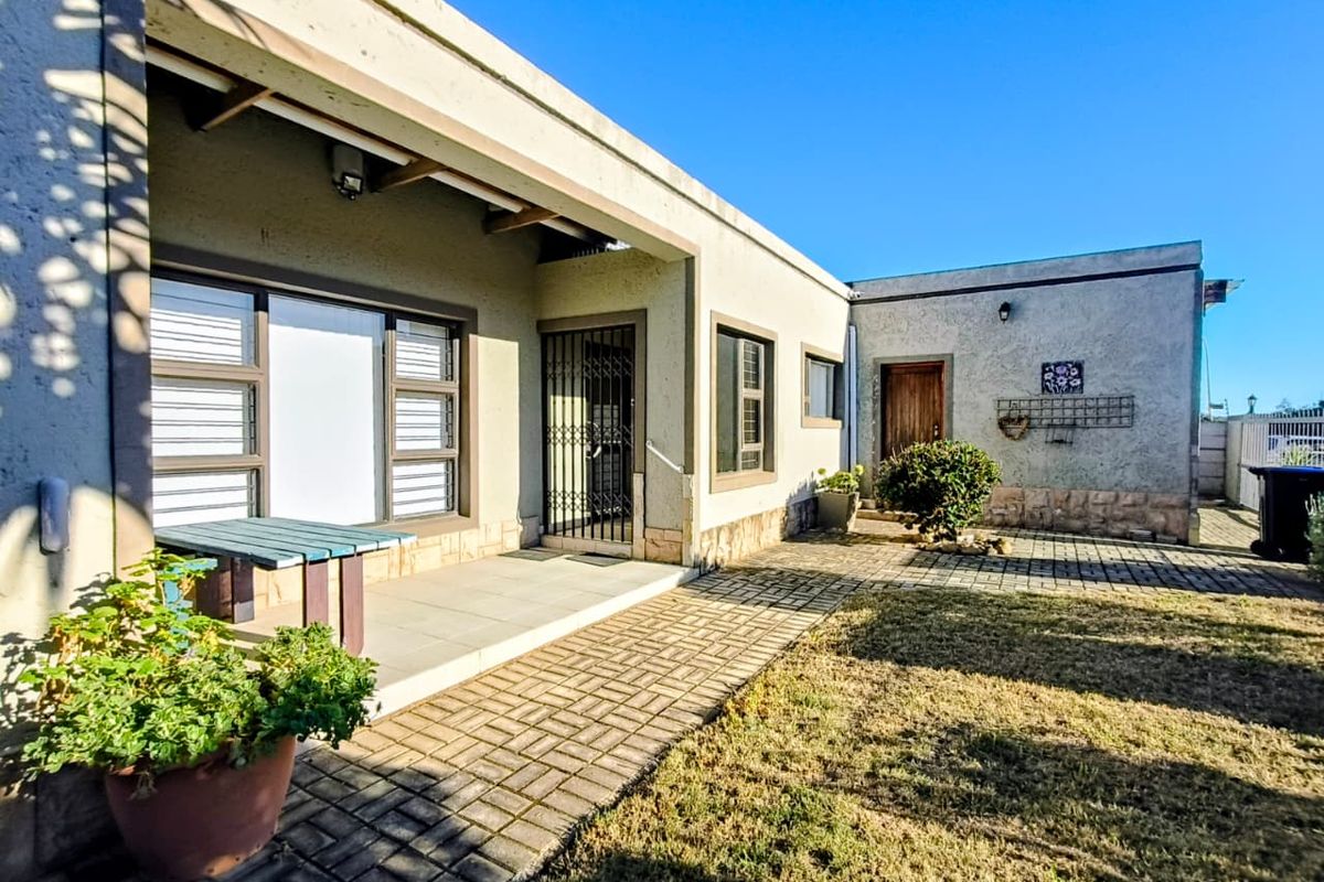 Rear exterior view featuring a paved patio area, security gate, and stone-clad accents, providing a functional outdoor space for the property.