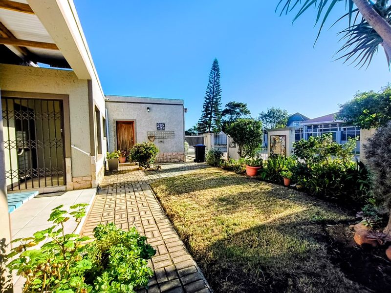 A rear exterior view featuring a paved walkway, a small lawn area, and a covered patio with a security gate.