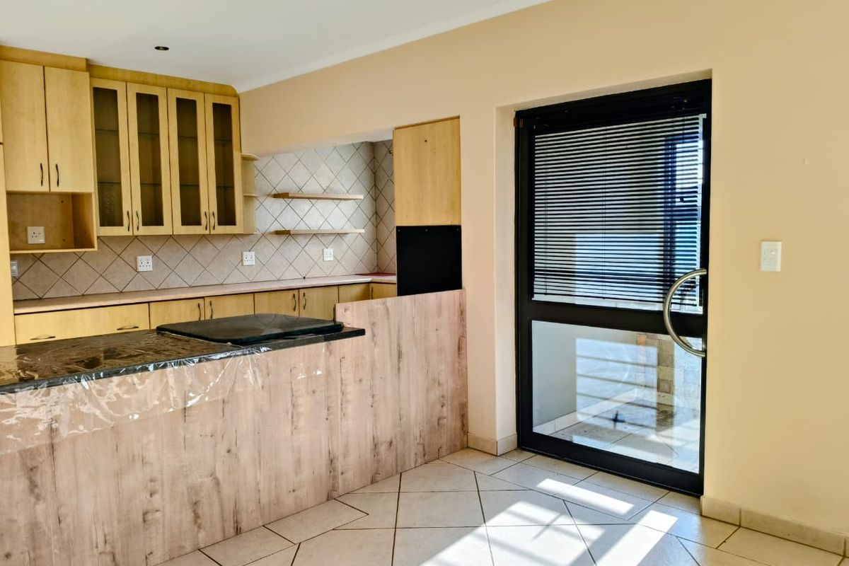 A functional kitchen featuring light wood-tone cabinetry, a dark countertop with integrated hob, tiled backsplash, and direct access to an outdoor area.