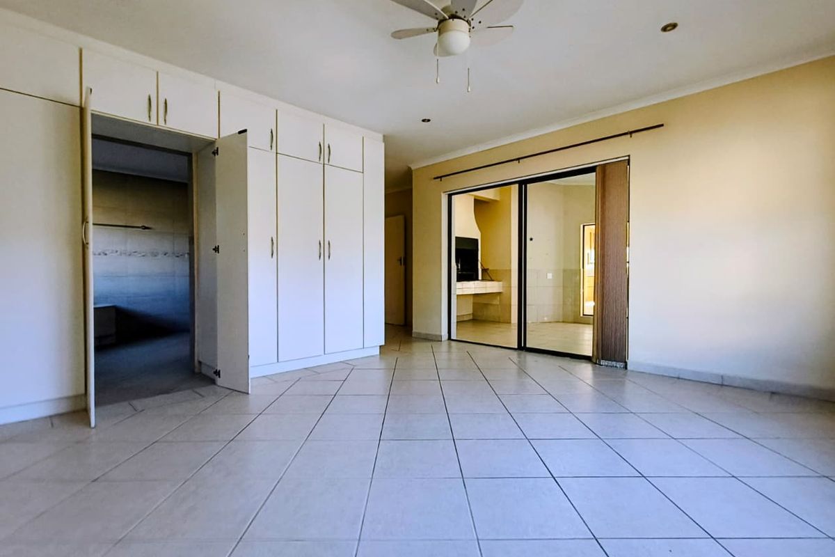 Spacious bedroom featuring neutral tiled flooring, extensive built-in cabinetry, a ceiling fan, and sliding glass doors leading to an adjacent area.