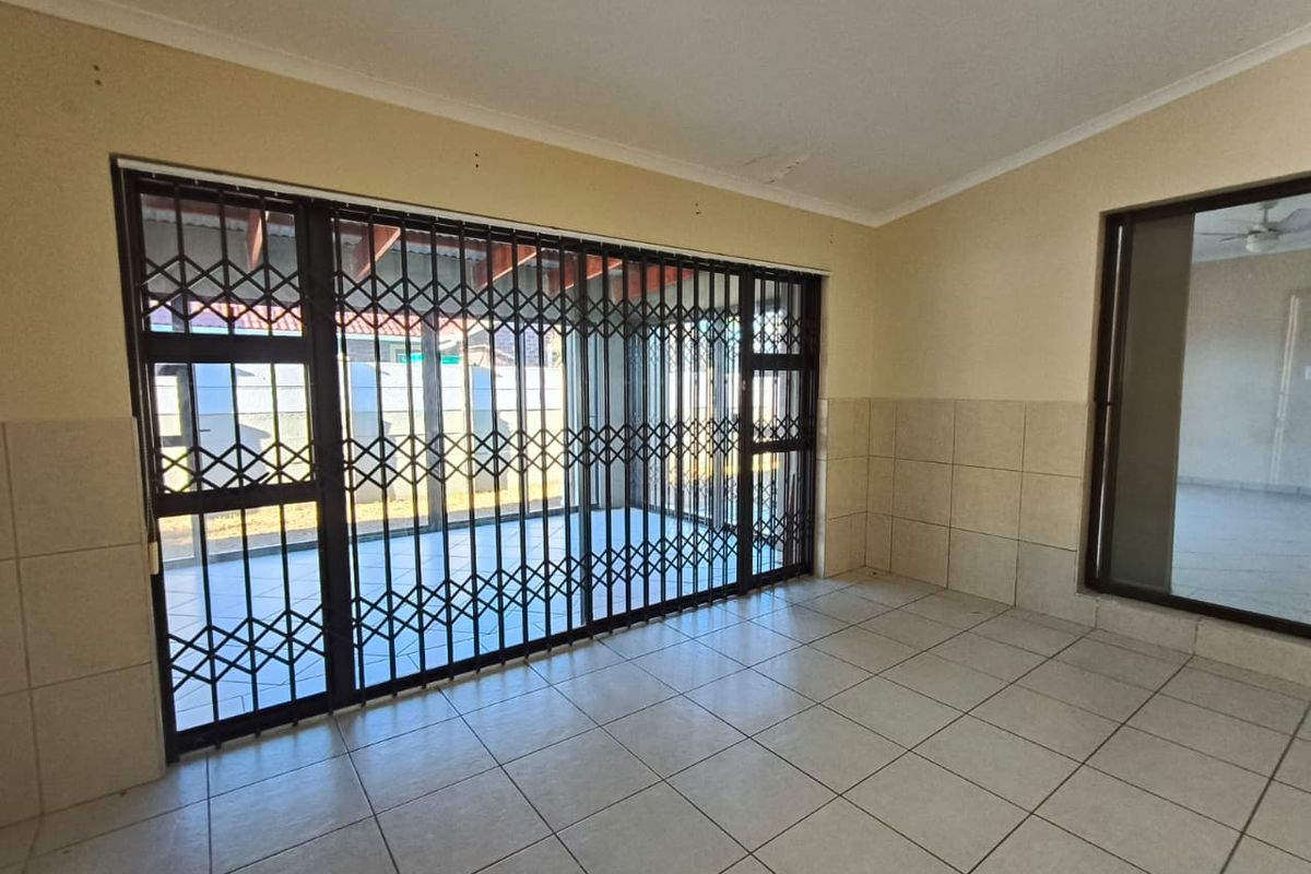 An empty living area featuring tiled floors, wall tiling, and a large sliding glass door with a security gate leading to the patio.