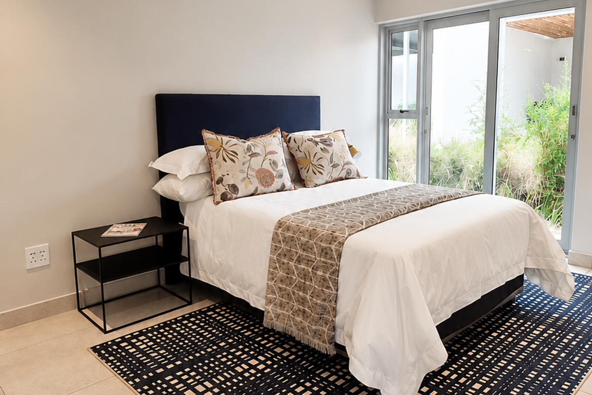 A bright, modern bedroom featuring neutral walls, large format floor tiles, and a sliding glass door providing direct access to the garden area.
