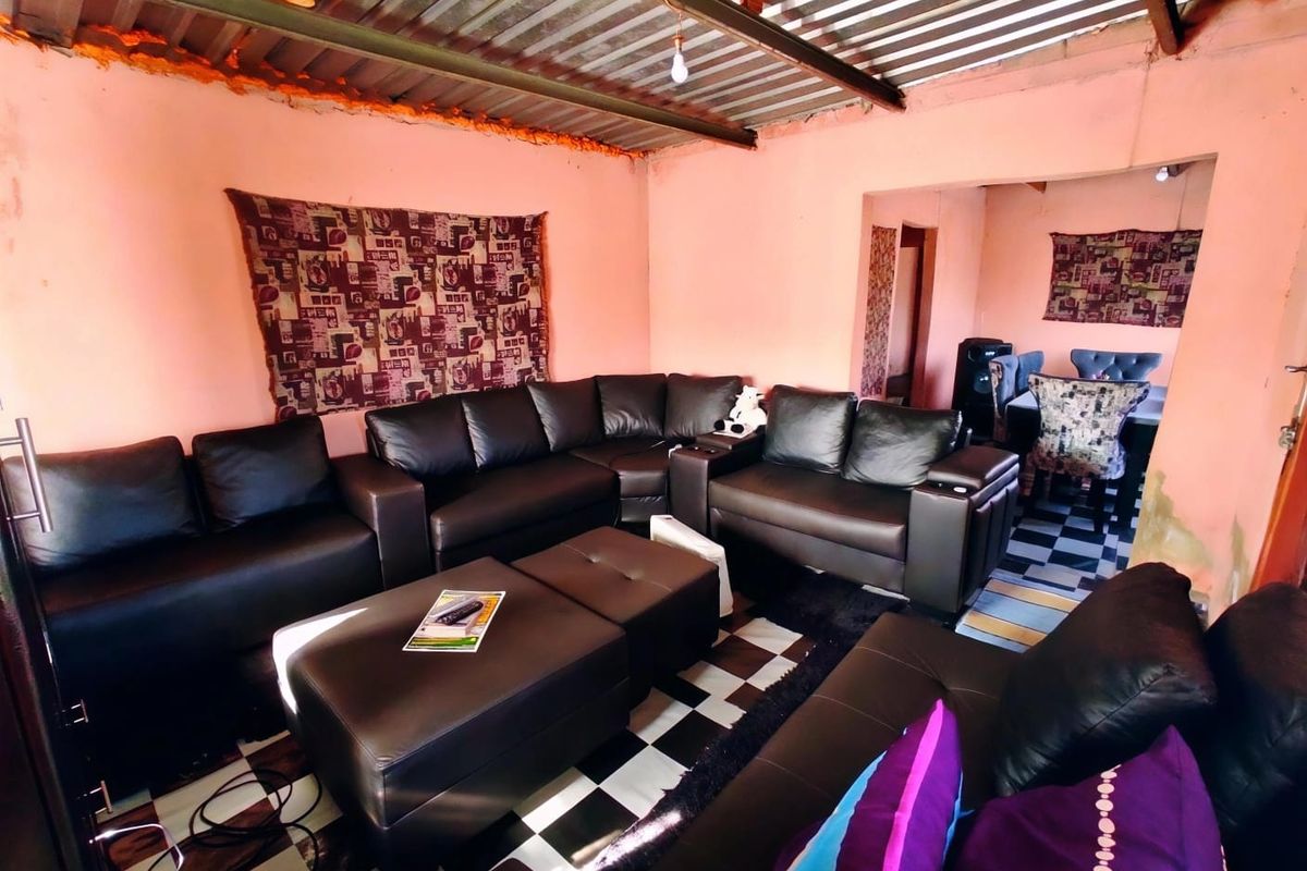 Living room area featuring checkered floor tiles and an exposed corrugated metal ceiling, requiring cosmetic updates to improve the overall finish.