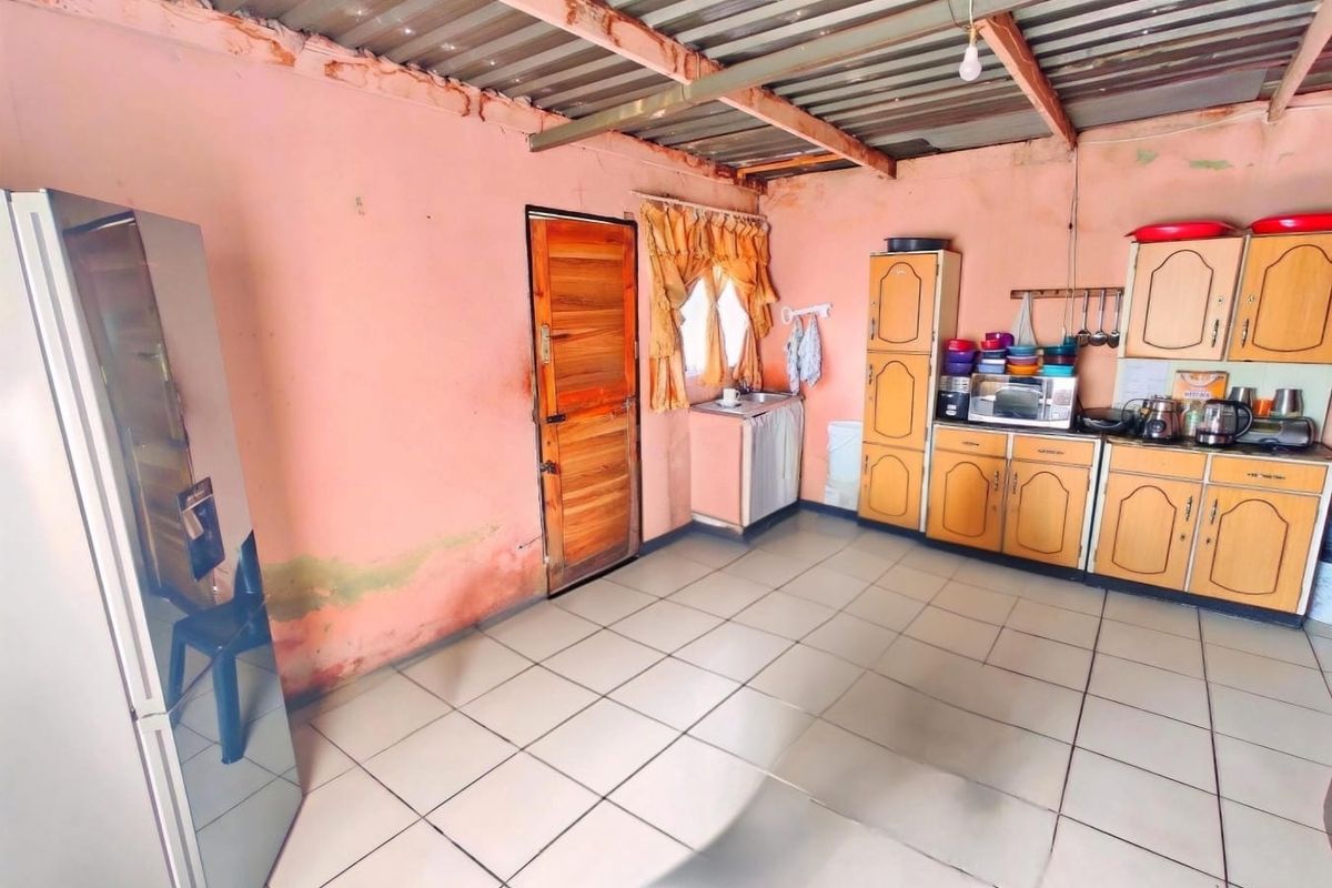 A functional kitchen space featuring fitted cabinetry and tiled flooring, currently requiring cosmetic updates and wall repairs to improve the overall condition.