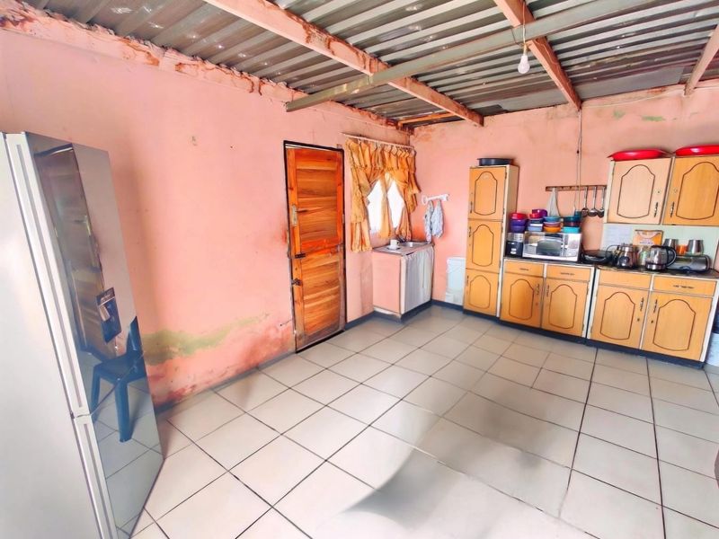 A functional kitchen space featuring fitted cabinetry and tiled flooring, currently requiring cosmetic updates and wall repairs to improve the overall condition.