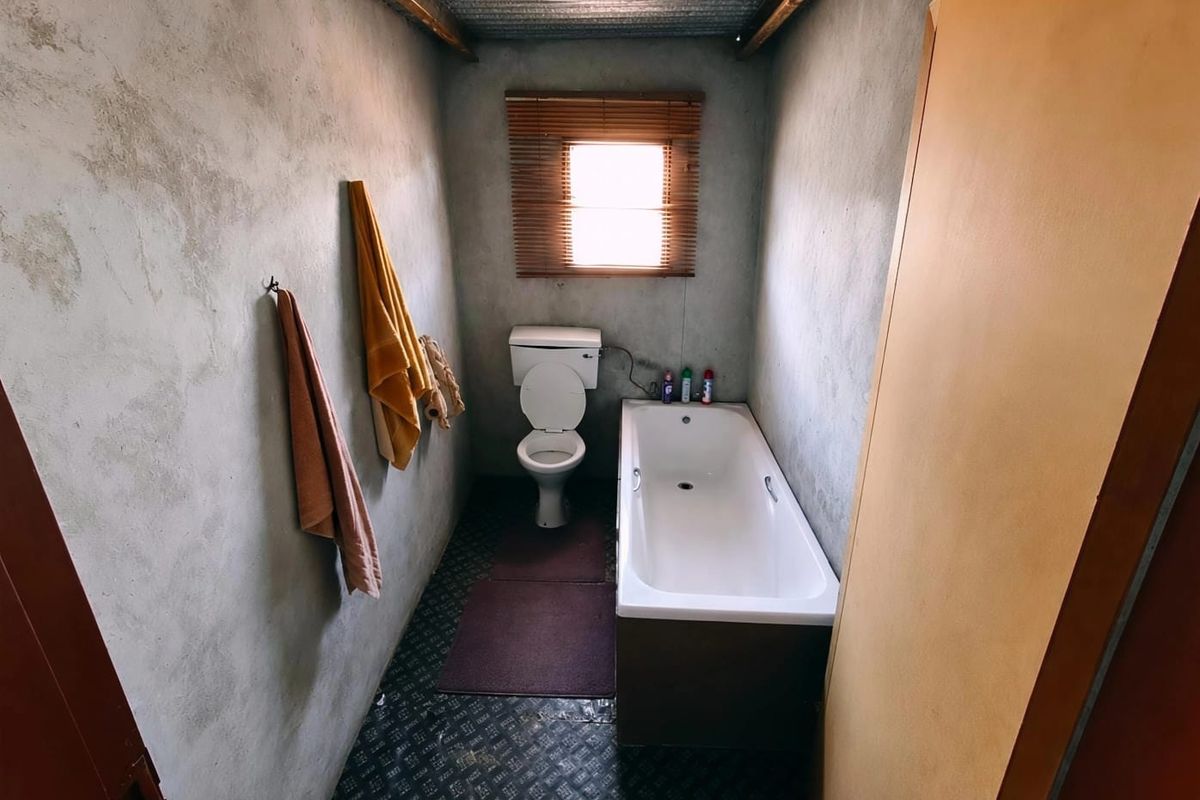 A compact bathroom featuring a bathtub and toilet with unfinished cement walls and a corrugated metal ceiling, requiring cosmetic updates.
