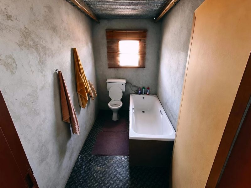 A compact bathroom featuring a bathtub and toilet with unfinished cement walls and a corrugated metal ceiling, requiring cosmetic updates.