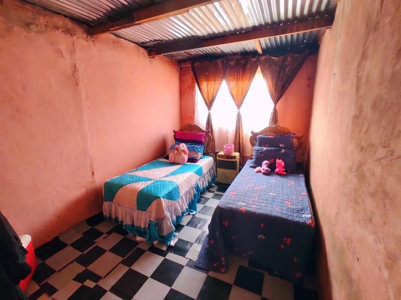A bedroom featuring a corrugated metal ceiling and checkered floor tiles, requiring significant cosmetic updates to the wall finishes.