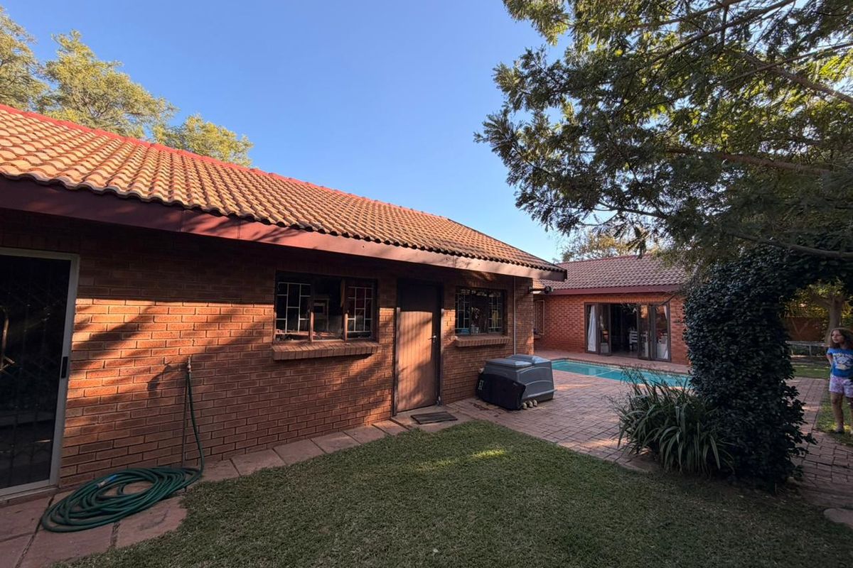 Rear view of the property featuring a brick facade, tiled roof, paved patio area, and a swimming pool.