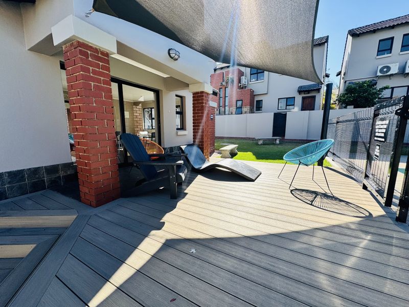 A well-maintained outdoor patio area featuring composite decking, brick support pillars, and a shade sail, providing a comfortable space for outdoor relaxation.